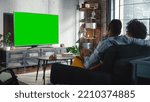 Small photo of Black Couple Sitting At Home in the Living Room During the Day and Watching Green Screen Chroma Key on Television Set, Relaxing on a Couch. Weekend Activities and Mainstream Media Concept.