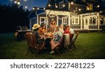 Small photo of Parents, Children and Friends Gathered at a Barbecue Dinner Table Outside a Beautiful Home with Lights Decorations. Old and Young People Have Fun and Eat Meals. Garden Party Celebration in a Backyard.