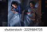 Small photo of Top View Bedroom Apartment: Young Woman Uses Smartphone in Bed at Night When Her Male Partner Trying to Fall Asleep Beside. Couple Fight, Argue. Social Media, Doom Scrolling, Fake News Addiction