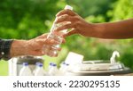 Small photo of Close Up of a Anonymous Person Handing Over a Water Bottle to Another Person. Green Background in Nature. Outdoors Fourt Court Selling Drinks. Ecology, Healthcare and Hydration Concept.