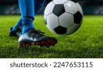 Small photo of Close-up of a Leg in a Boot Kicking Football Ball. Professional Soccer Player Hits Ball with Fierce Power and Scores Goal, Grass Flying. Beautiful Cinematic Low Angle Ground Artistic Shot