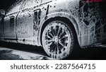 Small photo of Commercial Photo of a Black Electric SUV Covered in Washing Soap and Foam. Close Up Shot of Foam Dripping from Car's Rear Fender onto the Family Car's Tyre and Rim