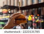 Man hand holding street food burger on festival blurred background . Street fast food concept. close up