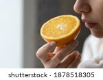 Sick woman trying to sense smell of  half fresh orange, has symptoms of Covid-19, corona virus infection - loss of smell and taste. One of the main signs of the disease. 