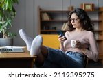 Woman freelance writer rest or procrastinate at workplace. Businesswoman in eyewear distracted from work on laptop scrolling social media on smartphone. Freelancer holding mobile phone and browsing