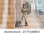 Small photo of Full-length of focused mature woman bookworm in library. Pensive middle-aged woman bibliophile with book enjoying reading, gaining knowledge from books, learning new skills. Lifelong Learning