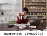 Small photo of Female artisan running small business analyzing bills and receipts while standing at table in ceramic art studio, doing pottery cost analysis, calculating fixed and variable costs of small business