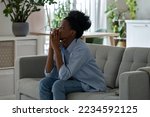 Small photo of Discouraged pensive African American woman looking into distance thinking about ways to solve financial problems. Frightened black girl sits on sofa in living room having lost mood due to inflation