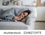 Sick exhausted woman lying on couch wrapped in blanket and coughs after being infected with dangerous flu or viral infection. Suffering unhappy girl with handkerchief and thermometer needs help doctor