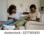 Small photo of Frowning single African American mother scolding naughty boy sitting on sofa at home. Misbehaviour of children. Annoyed angry mixed race woman think about punishment for mischievous spoiled ignore son