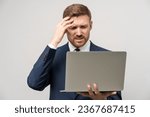 Small photo of Frustrated businessman in emotional stress watching downfall stock market on laptop, lost money on falling stock prices. Furious trader man in costume think about problem isolated on studio gray wall.