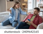 Small photo of Indignant, offended, hysterical woman screams at husband sitting on sofa with cellphone. Couple family quarrel conflict misunderstanding discord. Indifferent man ignores dissatisfied wife's questions.
