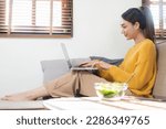 Ambitious Asian woman sitting on sofa working from home looking at tablet computer screen smiling Woman checking mail or searching the internet while communicating at home