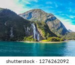 Travel New Zealand. Milford Sound, South Island, Fiordland National Park. Cruise scenic landscape view of high green reefs and waterfall, turquoise clear water, waves. Favourite tourist attraction.