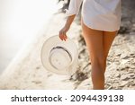 Young woman on a beach holdind white hat. Summer holiday concept travel. Young woman weared in White shirt on blured nature background. Summer story. Legs close up
