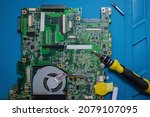 Small photo of Screwdriver and tweezers next to the dismounted motherboard. Repair of the old laptop, replacement of the fuse, determination of the cause of the failure.