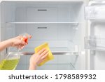 House cleaning - spray bottle with detergents for washing the fridge. Woman wipes the shelves of a clean refrigerator. Hands cleaning refrigerator.