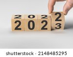 Small photo of happy new year concept, Flipping of wooden cube block change from 2022 to 2023. Wooden cube with flip over block 2022 to 2023 word. Business management, Inspiration to success ideas and goals.
