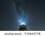Lighthouse beacon rays shining against starry sky and Milky Way
