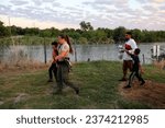 Small photo of Eagle Pass, TX, USA - Sept. 20, 2023: A Florida Park Commission agent on loan to Texas takes a Honduran migrant family that just illegally crossed the Rio Grande River to seek asylum into custody.