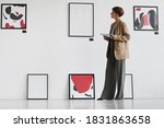 Small photo of Full length portrait of creative elegant woman looking at paintings hanging on white wall while visiting modern art gallery exhibition, copy space
