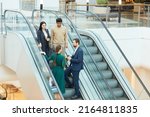 Wide angle view at group of business people standing on escalator in office building and communicating, copy space
