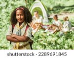 Small photo of Waist up portrait of cute black girl scout looking at camera while camping with school group, copy space