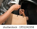 Small photo of Womanâ€™s driver driving thru hand pickup environmentally friendly craft brown paper bag out of a black car open window from seller meeting social distancing requirements and supporting small business