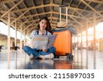 Small photo of Asian female passenger sitting and looking at a map In the platform at the train station, sitting waiting for the train, Asian woman with map, camera, sitting in the train station.