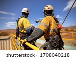 Small photo of Safe workplace trained supervisor with defocused an inertia reel shock absorbing hook fall arrest device clipping on the back safety harness hook while working at heights from 2m exposure open edges