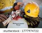Small photo of Safety workplace working at height permit book helmet personal locks place on the table with defocused inspector inspecting an inertia reel shock absorbing fall protection device prior used background