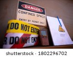 Small photo of Confined space warning sign permit entry by permit only and red barricade danger tape, yellow caution tape gas test leak atmosphere with defocused confined space permit book template, pen background