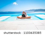 young woman at an luxury infinity swim pool looking out over the caldera of Santorini Greece, bright summer holiday Santorini poolside
