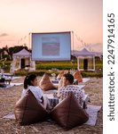 Small photo of A couple of men and women watching a movie at an outdoor cinema in Northern Thailand Nan Province out over the rice paddies in Thailand, green rice fields.