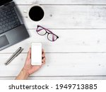 Laptop glasses coffee cup and two silver pen office workspace top view and hand hold smartphone white screen copy space