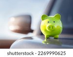 Small photo of Green piggy bank money box on top of car bonnet, concept for new vehicle purchase, insurance or driving and motoring cost