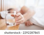 Glass of fresh drinking water on bed bedside table man thirsty reaching hand