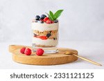 Sweet dessert in a glass with berries, mint, whipped cream and biscuit on a wooden board. Healthy food, vegan, sugar, gluten and lactose free. Berry dessert, cheesecake, trifle, mouse in a glass.