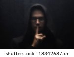 Small photo of A man in a black hood and glasses gesturing silence. Scary man standing behind a transparent plastic. Concept for threat, violence, danger, menace.