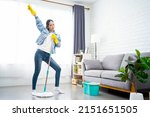 Small photo of Happy woman sings while cleaning the living room using a mop as a microphone. She had fun while doing housework.