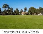 Small photo of Vacant green grassy sports ground in a public local park in an Australian suburban neighbourhood. Background texture of grass lawn with some residential houses in the distance.