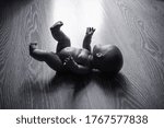 Small photo of Baby doll on a wooden floor, symbol of abortion, dead child, miscarriage, bygone childhood. Black and white dramatic scene.