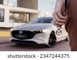 Small photo of Berlin Germany 14 August 2023 Fourth-generation Mazda 3 compact car ,Front and side view (hatchback). Model year 2023. Stands on road front of modern house. Sunset lense flares. Mazda Key in hand.