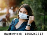 Young brunette beautiful women in city street or park weared with face mask that protect against the spread of corona virus disease or SARS-CoV-2. Social distancing during pandemic COVID 19.