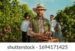 Small photo of Portrait of proud caucasian farmer in strawhat smiling with joy holding large basket of grapes working during harvest in vineyard.