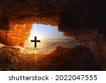 Small photo of Black cross with bright light in front of dark cave in the dry hostile desert with boulders