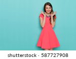 Smiling beautiful young woman in pink mini dress posing with hands on chin. Three quarter length studio shot on turquoise background.