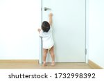 Small photo of 1 year old toddler Asian baby boy standing on tiptoes reaching up try to open door knob,Security and Safety Child Concept.