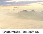 Greylag goose (Anser anser), wild geese in flight, with cloud-covered mountain landscape at sunset