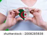 Woman in white t-shirt holds a heart in the form flag Algeria on her chest. Photo for a postcard on Flag Day, Independence Day, travel, patriotism, other holiday